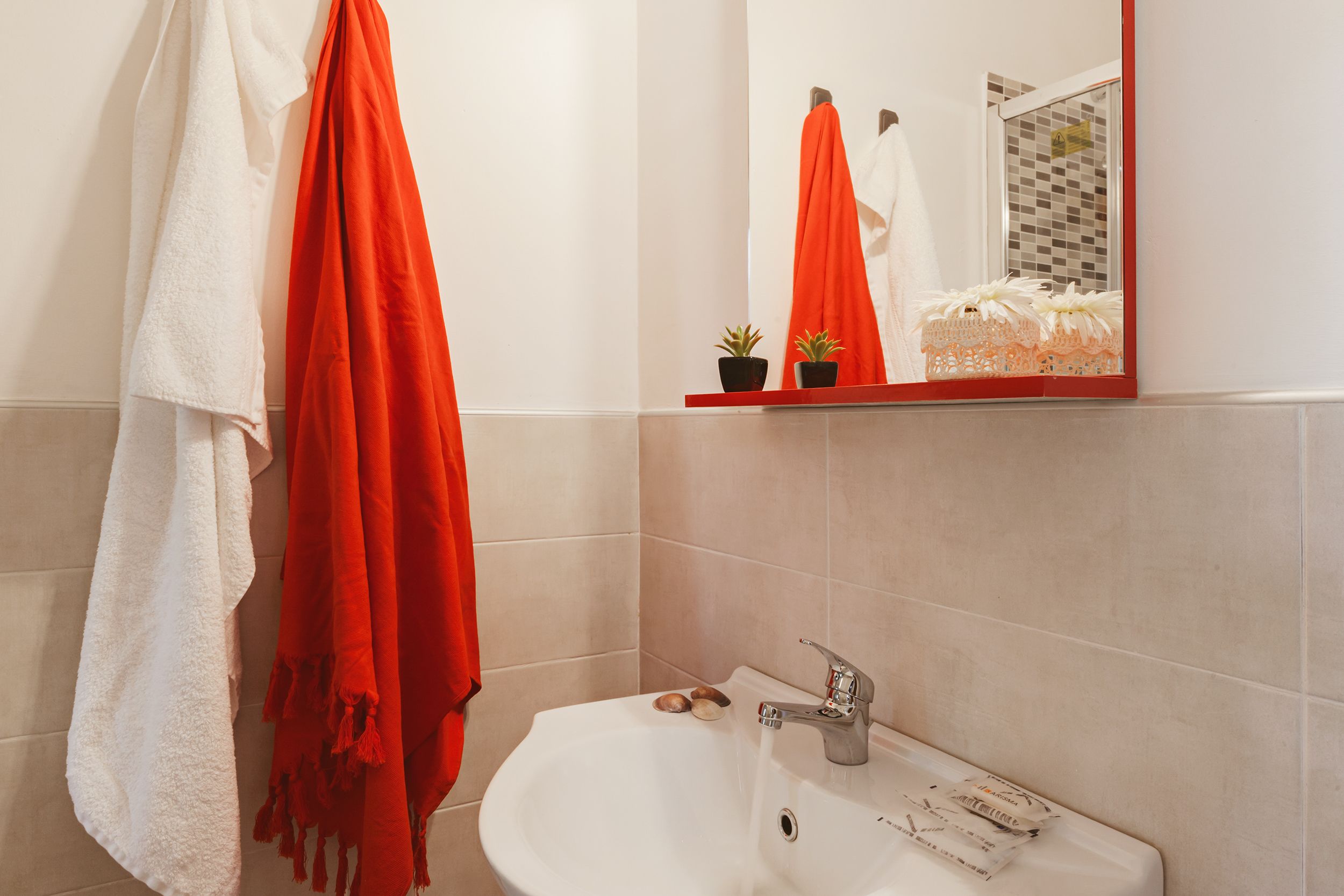 A bathroom with a white sink, a mirror, and two towels, one white and one orange.