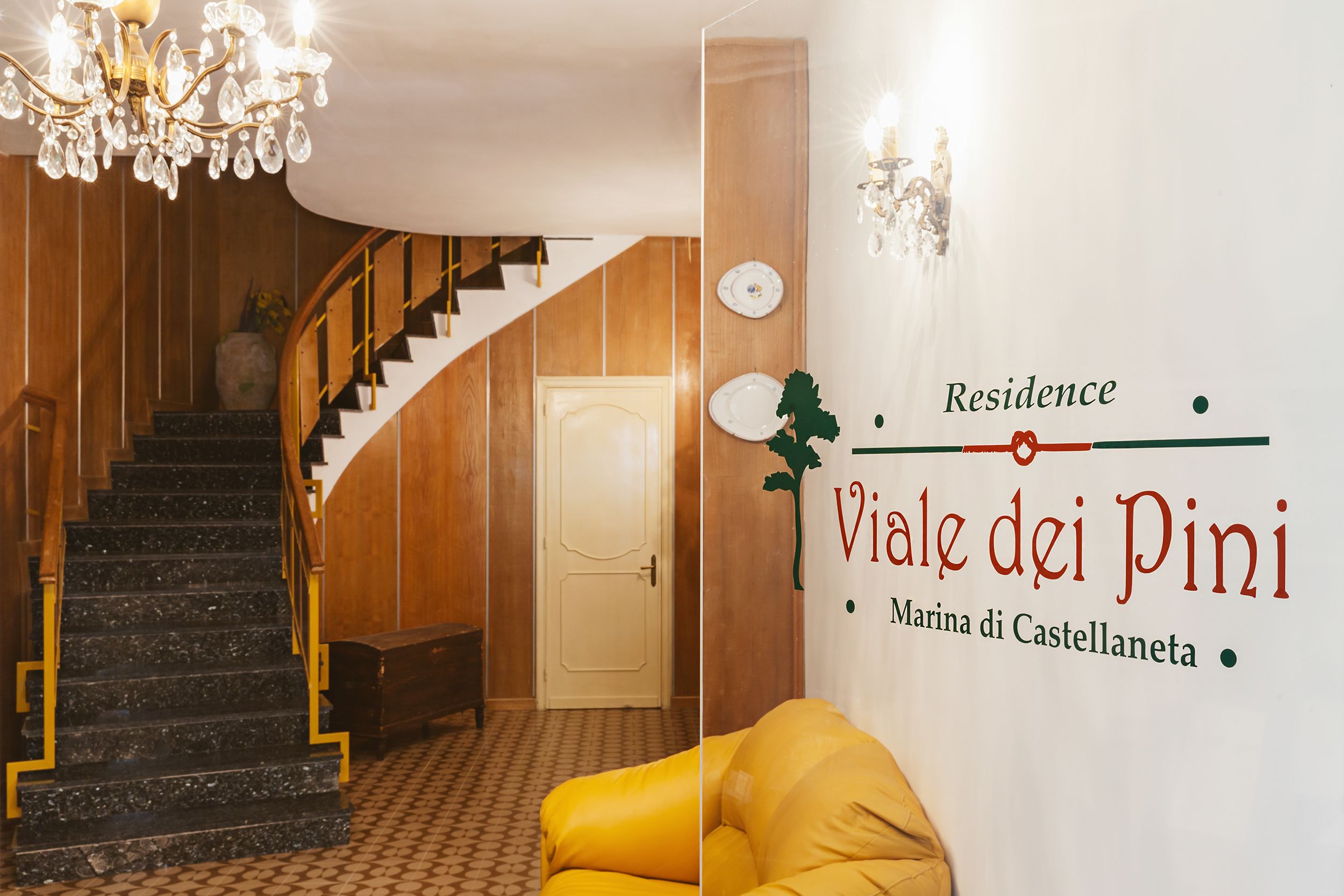 Portaat, jotka johtavat ovelle, kattokruunu ja seinä, jossa on kyltti, jossa lukee: ”Residence Viale dei Pini Marina di Castellaneta”.