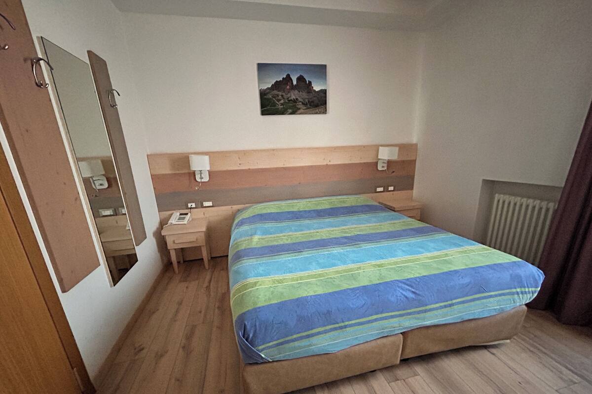 A hotel room with a bed, a nightstand, a telephone, a mirror, and a painting on the wall.