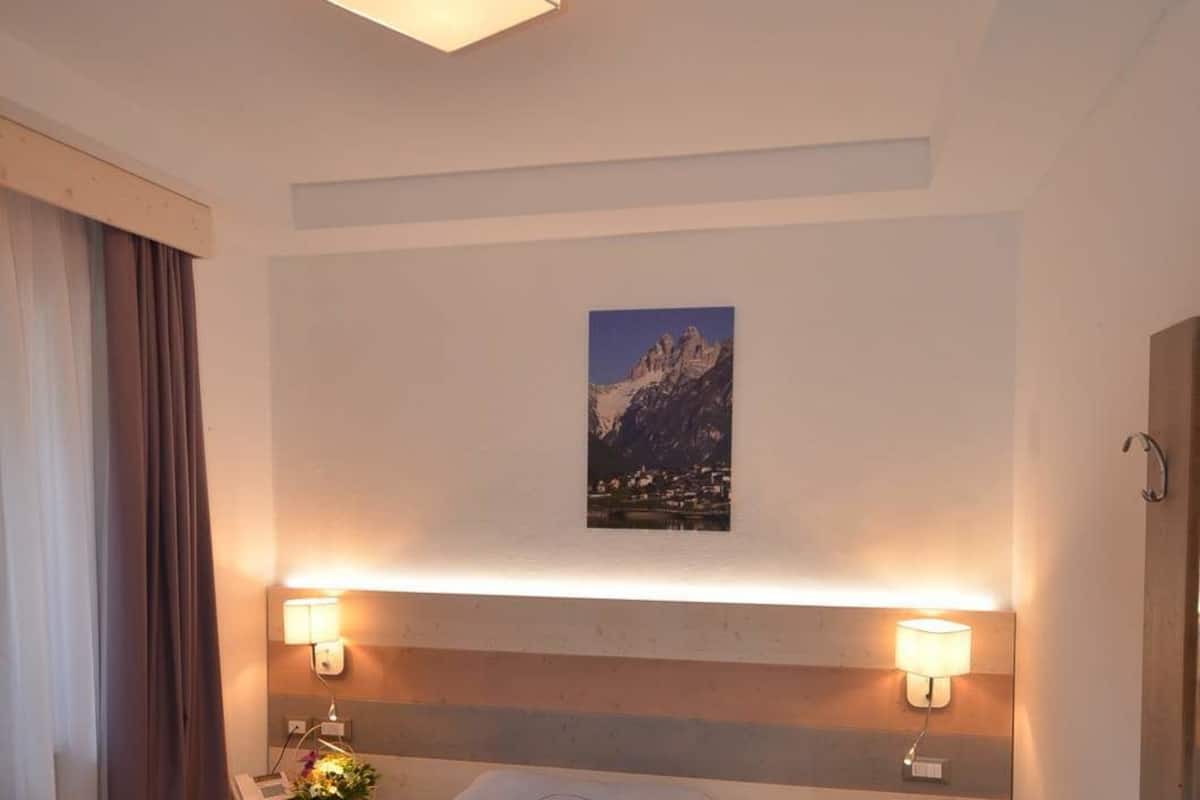 A hotel room with a bed, bedside lamps, a painting, and a wooden floor.