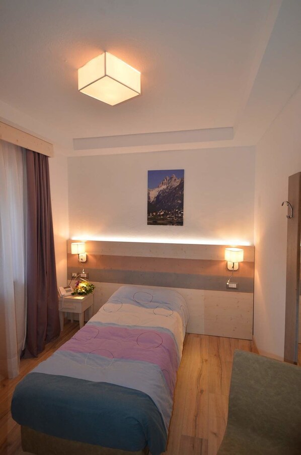 Una habitación de hotel con cama, lámparas de noche, un cuadro y suelo de madera.