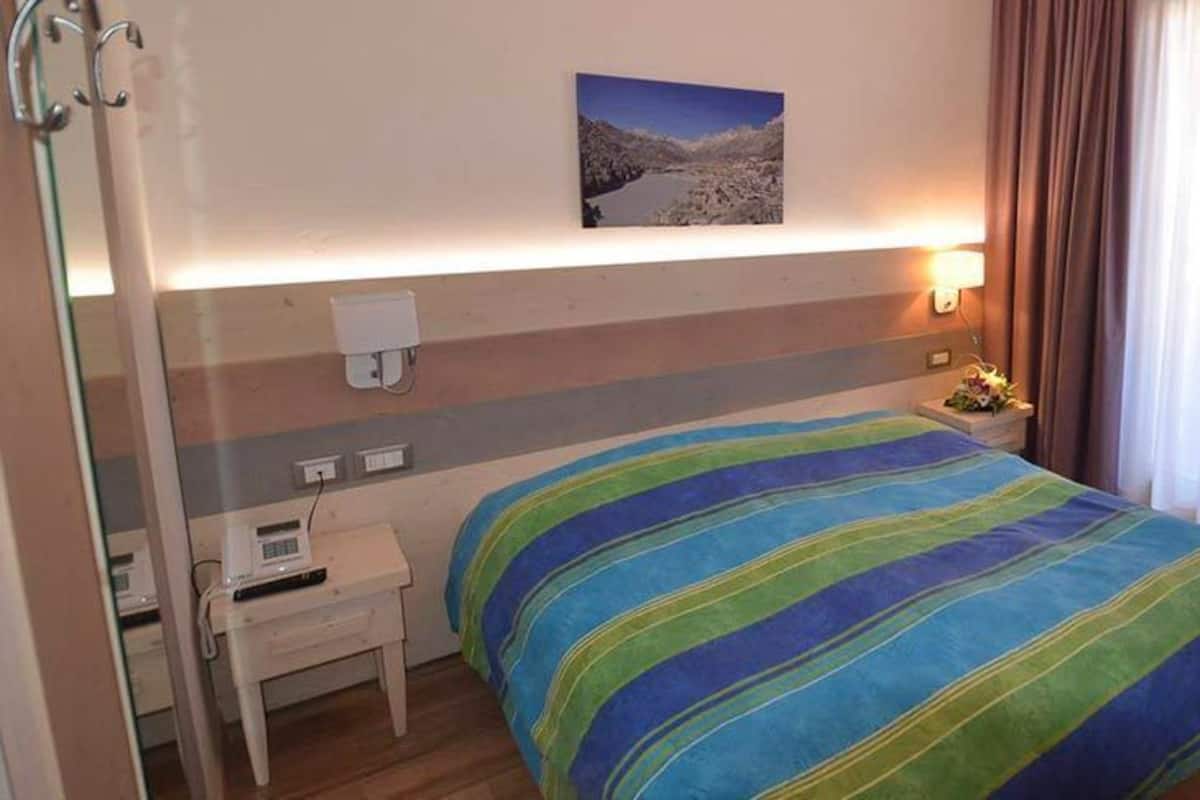 A hotel room with a bed, bedside table, lamp, and a painting on the wall.
