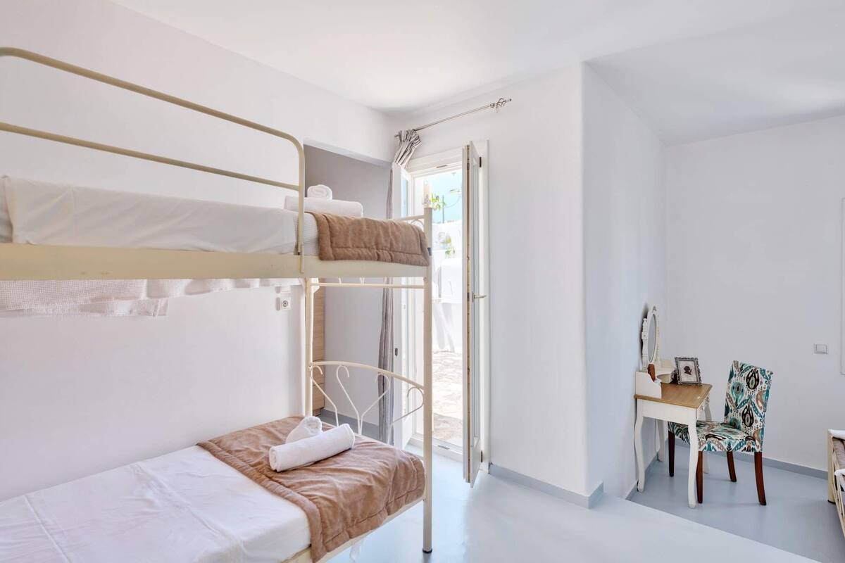 Habitació amb lliteres, escriptori, cadira, finestra i porta que dona a l'exterior.
