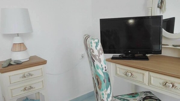 A room with a wooden desk, a computer monitor, a patterned chair, and a lamp.