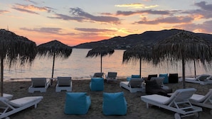 Une plage avec des chaises longues et des parasols, une mer calme et un coucher de soleil sur les collines.
