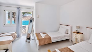 Une chambre à coucher comprenant un lit, une chaise, une table de chevet, une lampe et une vue sur la mer par une fenêtre.