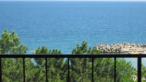 A coastal view with a rocky shoreline and dense green trees in the foreground. - Semiramis Hotel (Saturn)