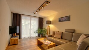 A modern living room with a sofa, a coffee table, a TV, and a lamp. - Matterhorngruss Apartments (Zermatt)