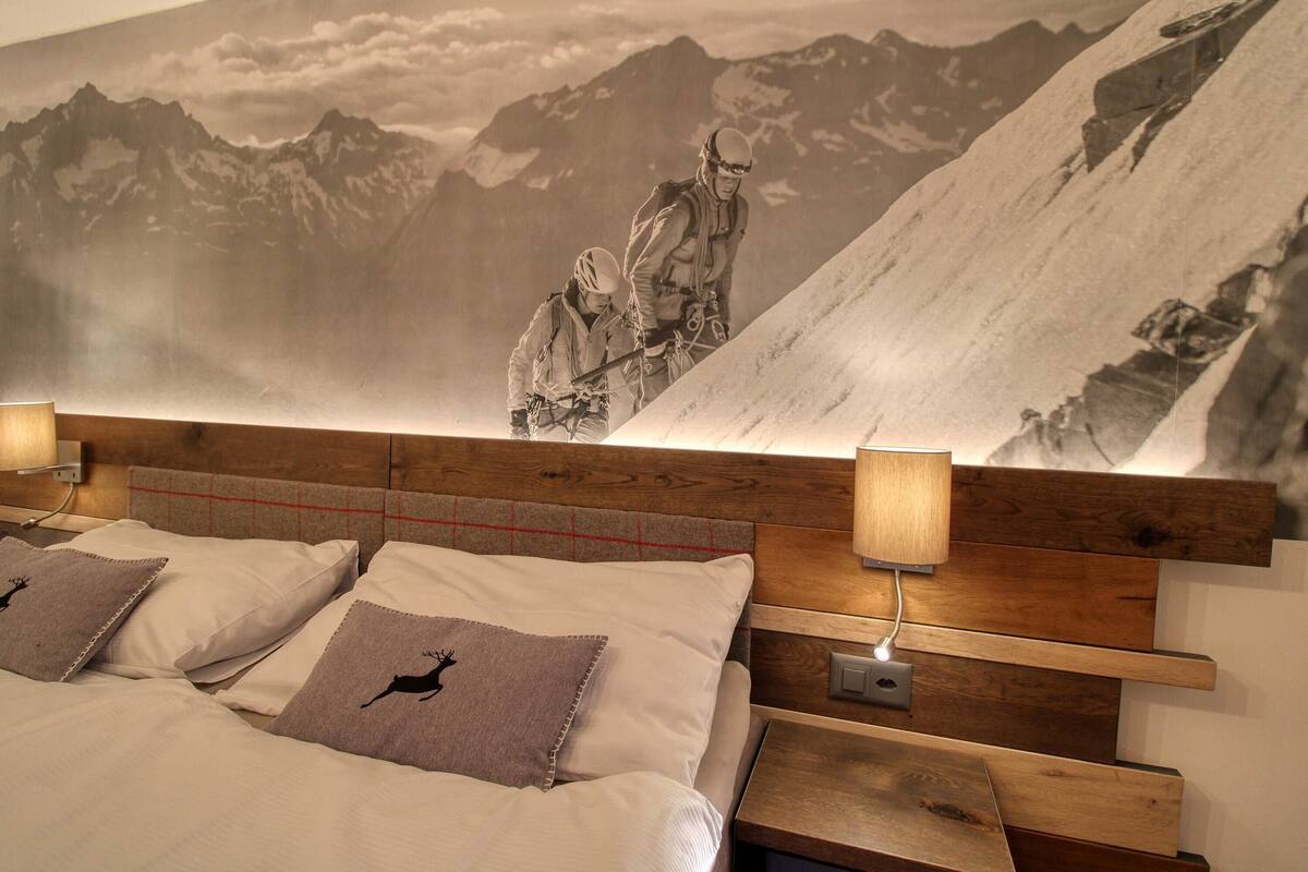 Een slaapkamer met een wanddecoratie van bergen, een houten hoofdeinde en twee bedlampjes.