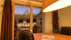 A dining area with a wooden table, a magazine, and a view of a mountain through a glass door. - Matterhorngruss Apartments (Zermatt)