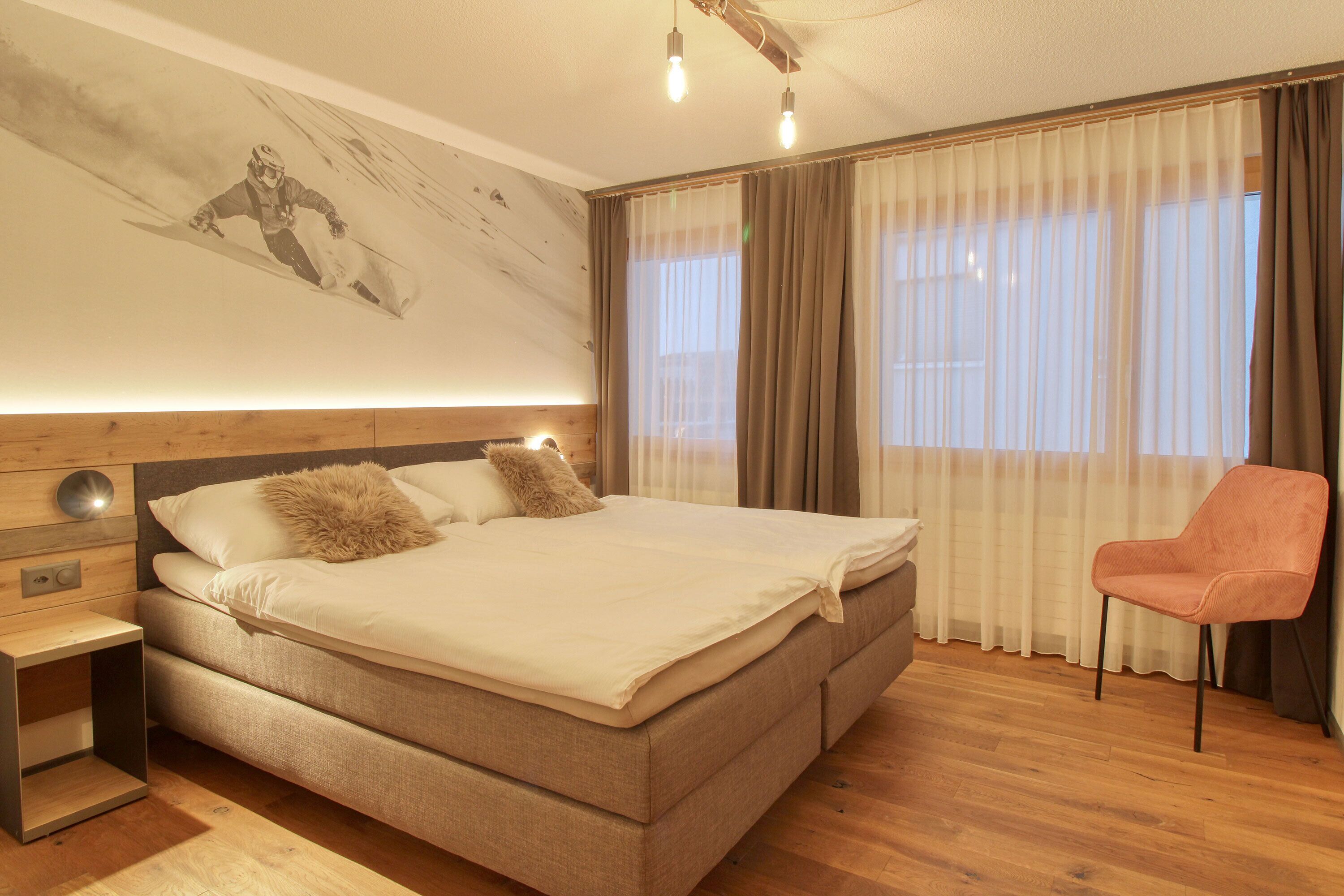 A bedroom with a large bed, a nightstand, a chair, and a wall mural.