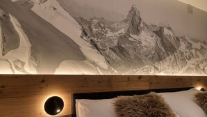 A bedroom with a large mountain mural, a wooden headboard, and a fur throw pillow. - Matterhorngruss Apartments (Zermatt)