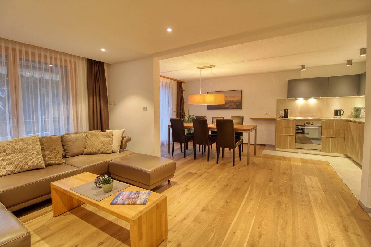 Een moderne woonkamer met een bank, salontafel en een eethoek met stoelen en een tafel.