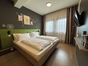 A hotel room with a double bed, a TV, a bookshelf, and a wall with decorative elements. - JUFA Hotel Graz Süd - Self Check-in (Graz)