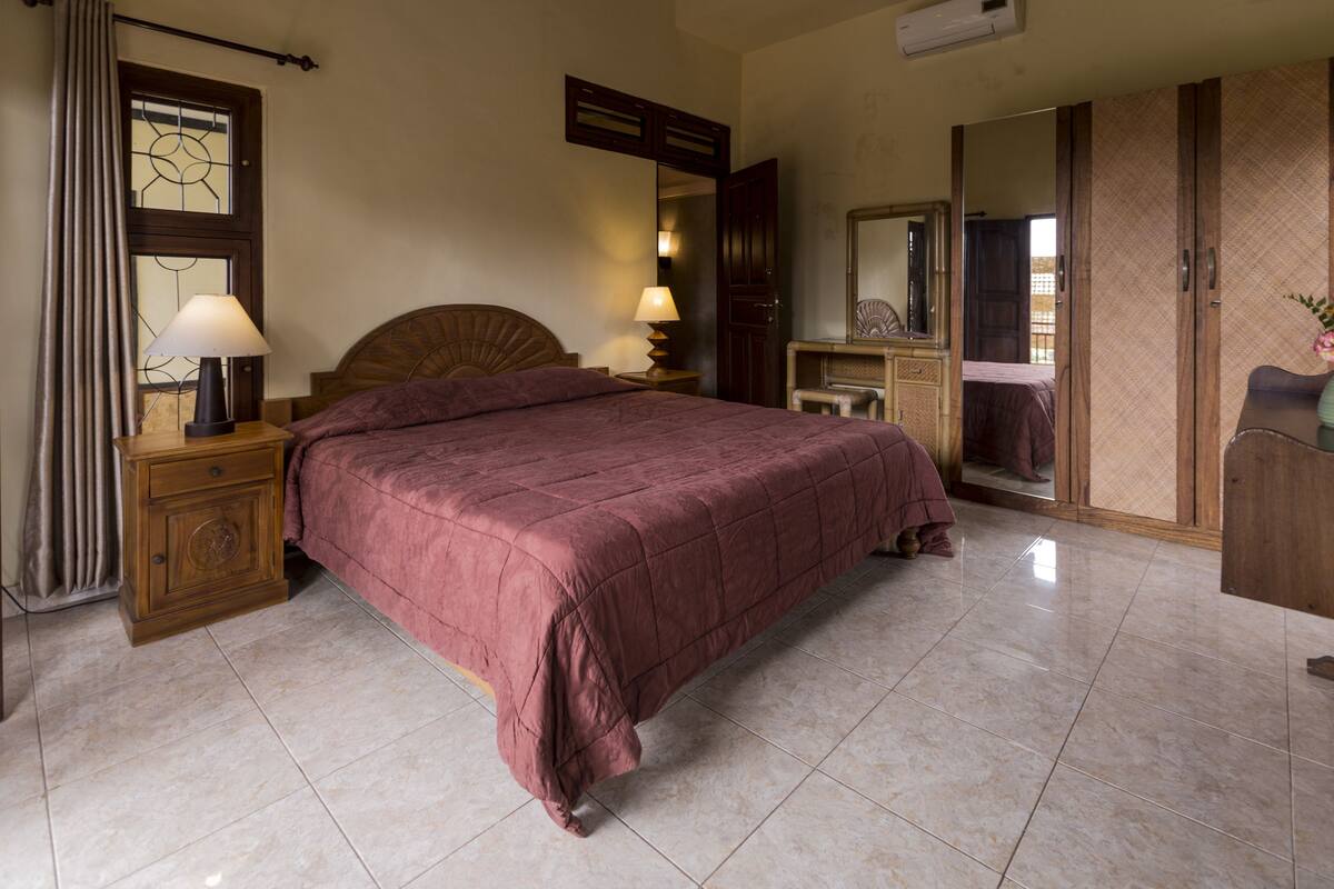 A bedroom with a large bed, two bedside tables with lamps, a wooden headboard, a dresser, and a mirror.