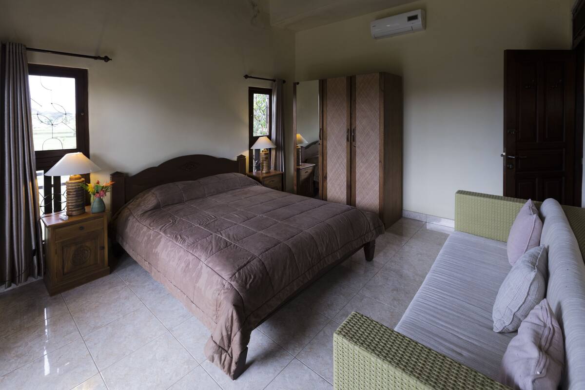 A bedroom with a large bed, a nightstand with a lamp, a wardrobe, and a window with curtains.