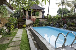 A swimming pool with a stone border, surrounded by lush greenery and a small garden. - Murni's Villa Ligondi (Ubud)