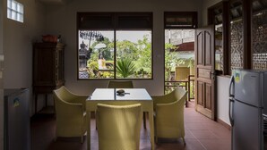A kitchen with a dining table, wicker chairs, a refrigerator, and a window with a view of greenery. - Murni's Villa Ligondi (Ubud)