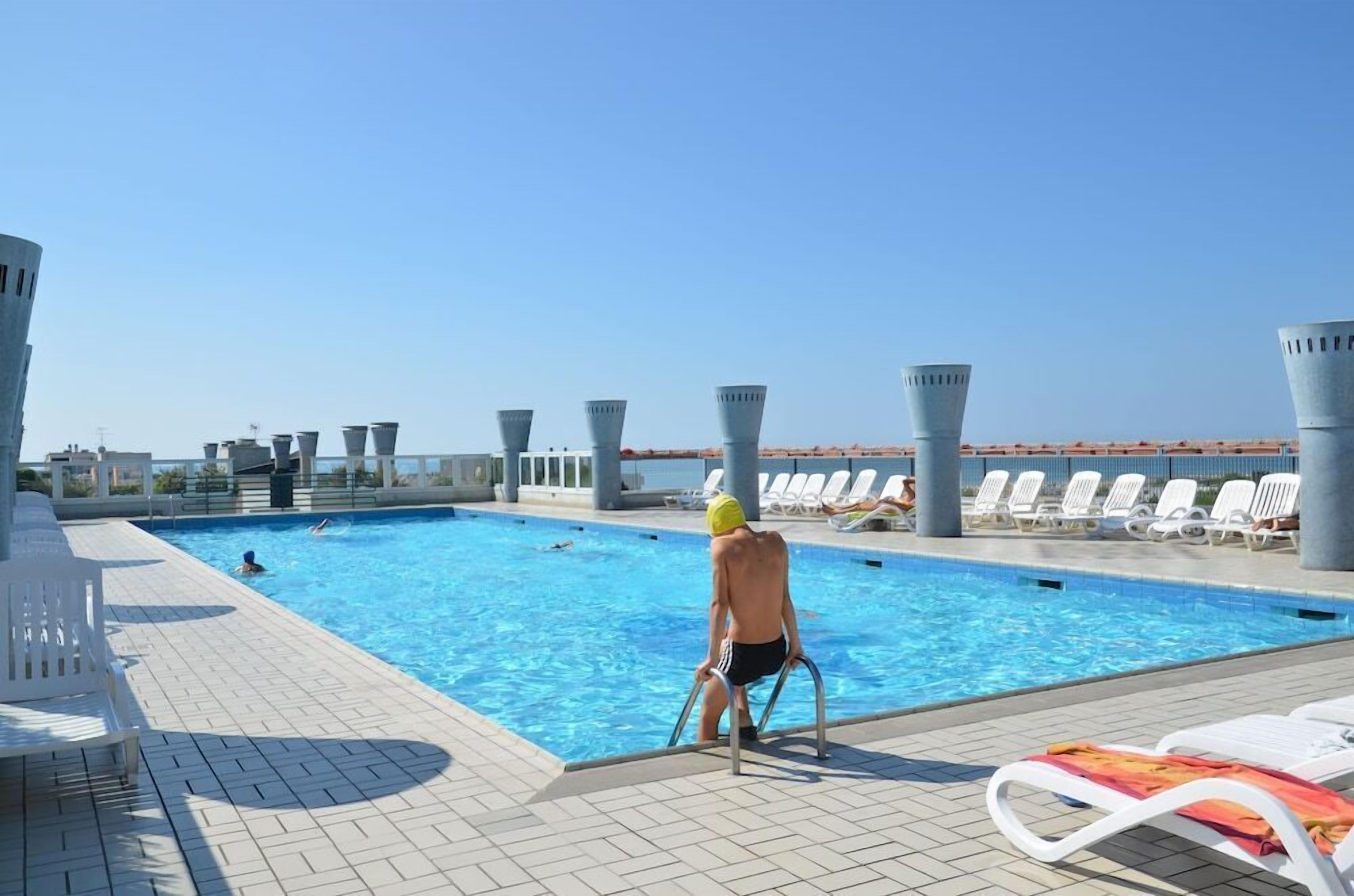 A swimming pool with lounge chairs and a person in swimwear.
