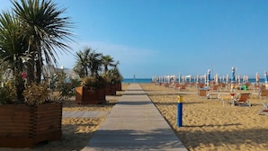 Ein Strand mit einer Holzpromenade, Palmen und Liegestühlen.