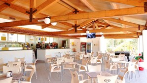 Una cafetería con vigas de madera, sillas blancas y una barra con la carta.