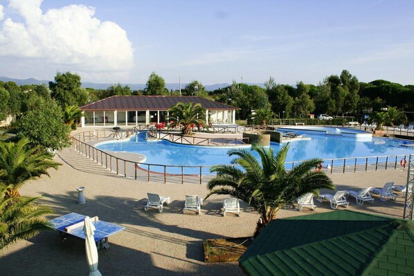 A swimming pool with lounge chairs and a building with a tiled roof. - Camping Le Palme (Bibbona)