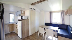 Una kitchenette compacta con refrigerador, microondas y gabinetes de madera. Hay una zona de comedor con una mesa y sillas, y un sofá azul.