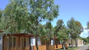 Un hilera de casas móviles de madera con balcones, rodeadas de árboles y un cielo despejado.