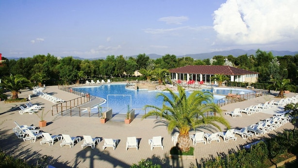 Un resort con una amplia piscina, tumbonas y un edificio de techo rojo.