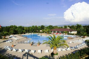 A resort with a large swimming pool, sun loungers, and a building with a red roof. - Camping Le Palme (Bibbona)