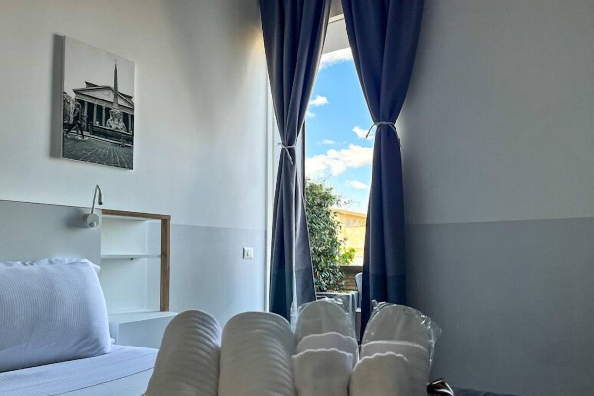 A hotel room with a bed, a window with curtains, a wall-mounted artwork, and a view of the outside.