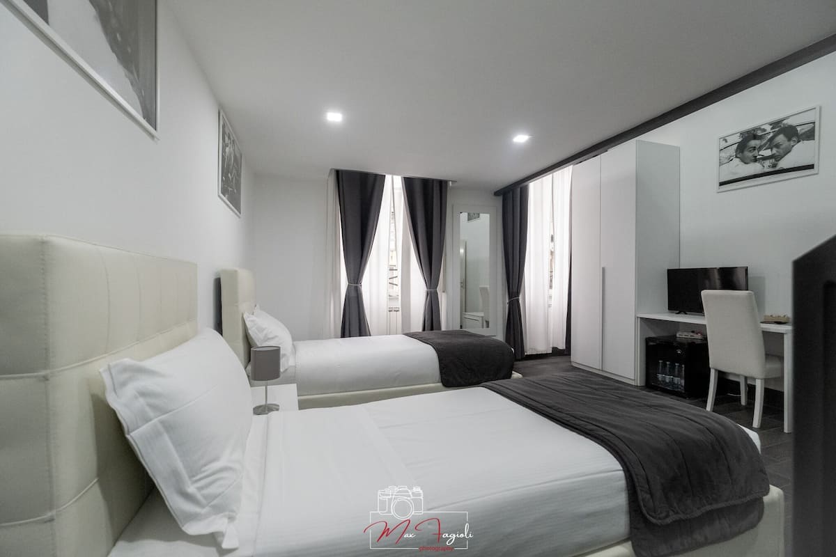 A modern hotel room with two beds, a desk, a chair, a TV, and a wardrobe.