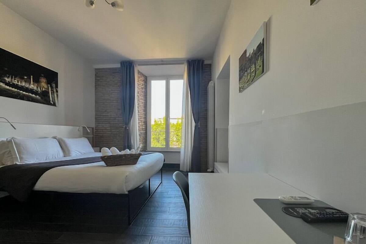 A modern hotel room with a bed, a desk, and a window with curtains.