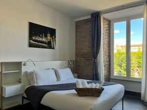 A hotel room with a large bed, a headboard, a nightstand, a window with a view of greenery, and a wall-mounted picture. - Arch Rome Suites (Rome)