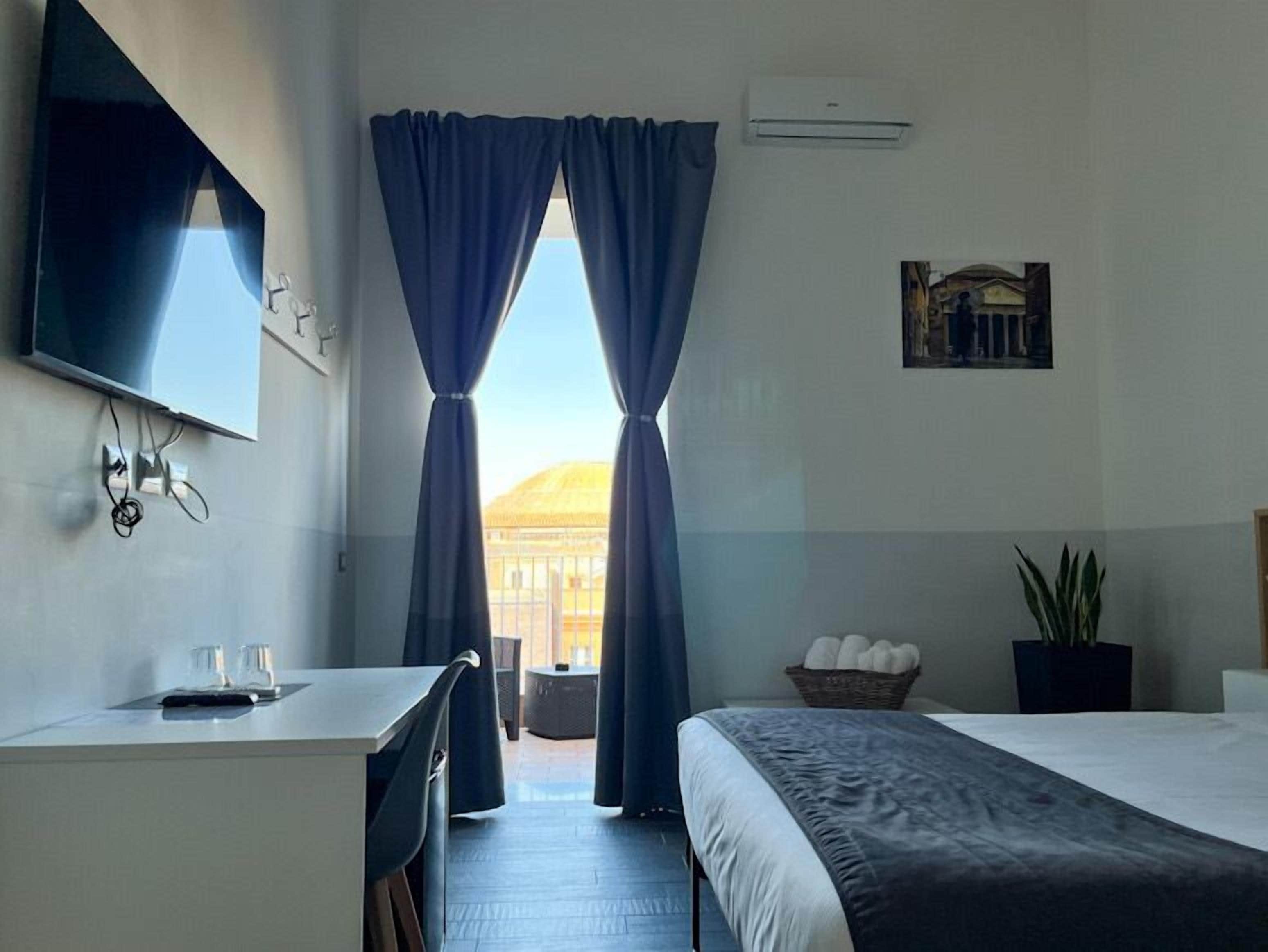 A hotel room with a bed, a desk, a chair, a TV, and a window with curtains.