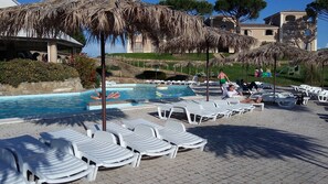 A pool area with lounge chairs and umbrellas, a swimming pool, and a building in the background.