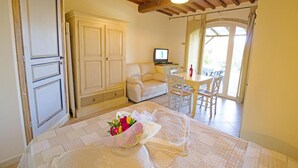 A cozy room with a bed, a desk with a computer, a dining area with chairs, and a large window.