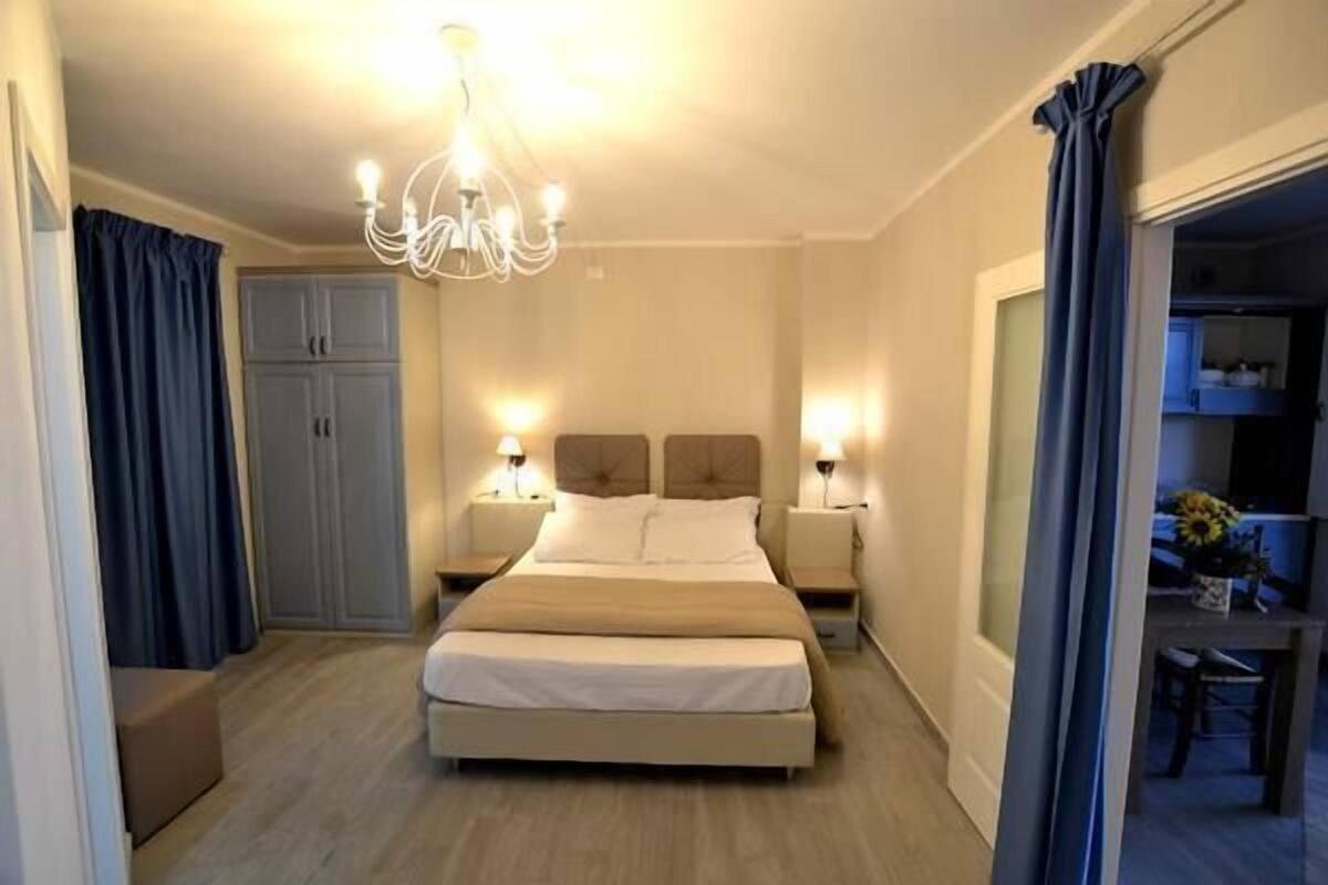 Une chambre d’hôtel avec un grand lit, deux tables de chevet avec des lampes, un lustre, une armoire et une vue sur la salle à manger.