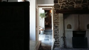 Quarto com lareira de pedra, uma mesa de madeira com uma cadeira e vista para uma escadaria de pedra que dá para outro quarto.