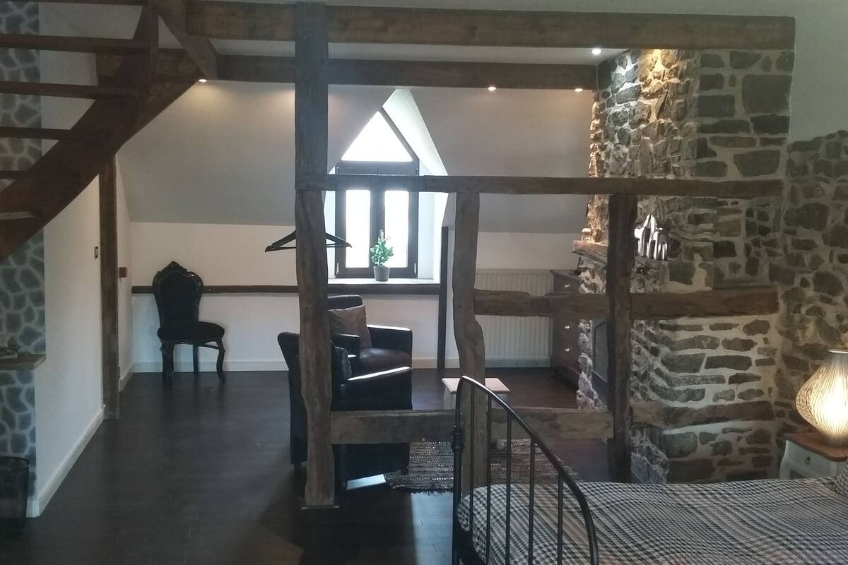 A spacious loft with exposed wooden beams, a stone wall, and a cozy seating area with a patterned sofa and a small table.