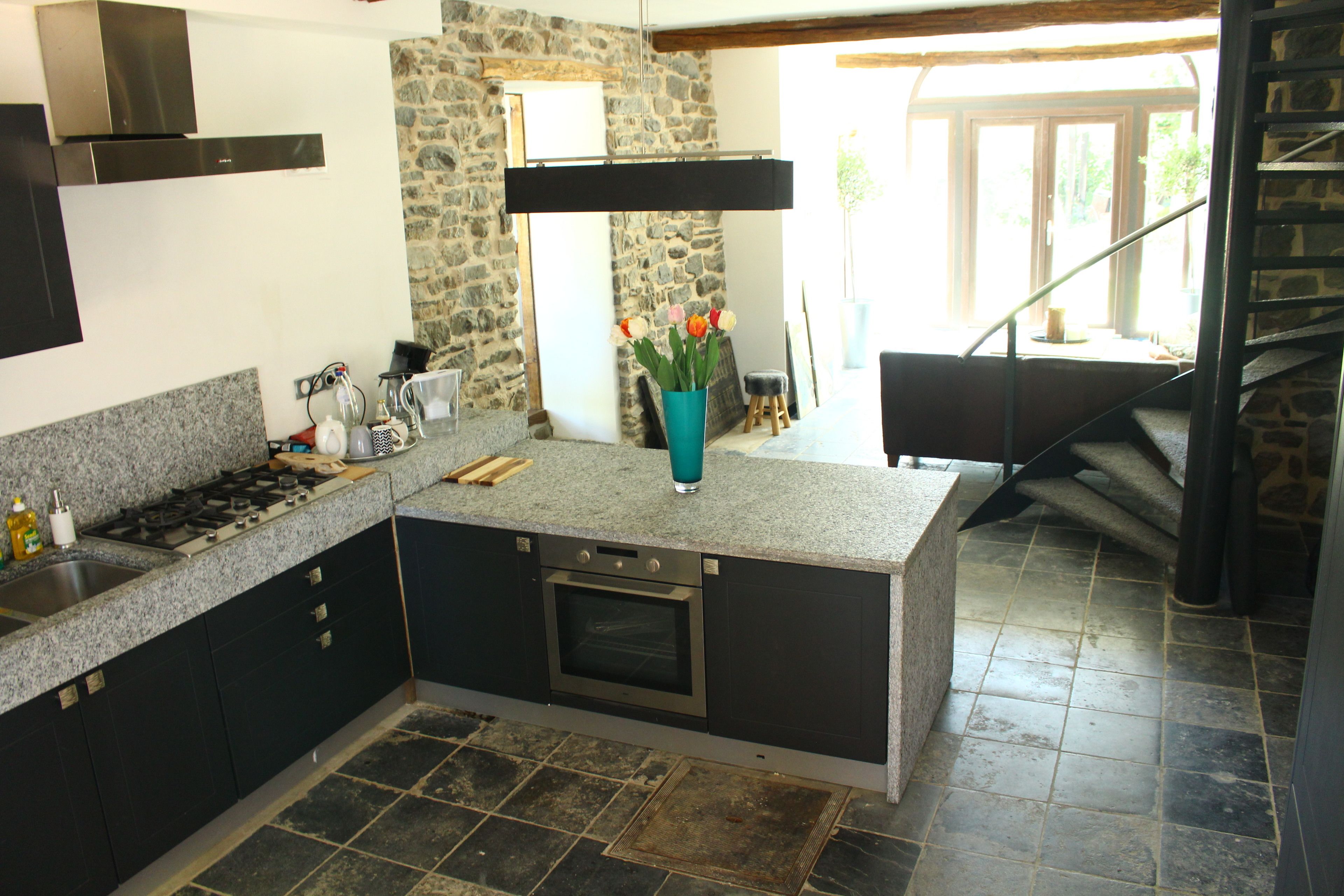 Uma cozinha moderna com bancadas de granito, forno embutido e parede de pedra.