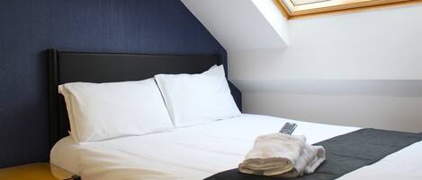 A neatly made bed with white linens and a black throw blanket, a bedside table, and a framed notice on the wall.
