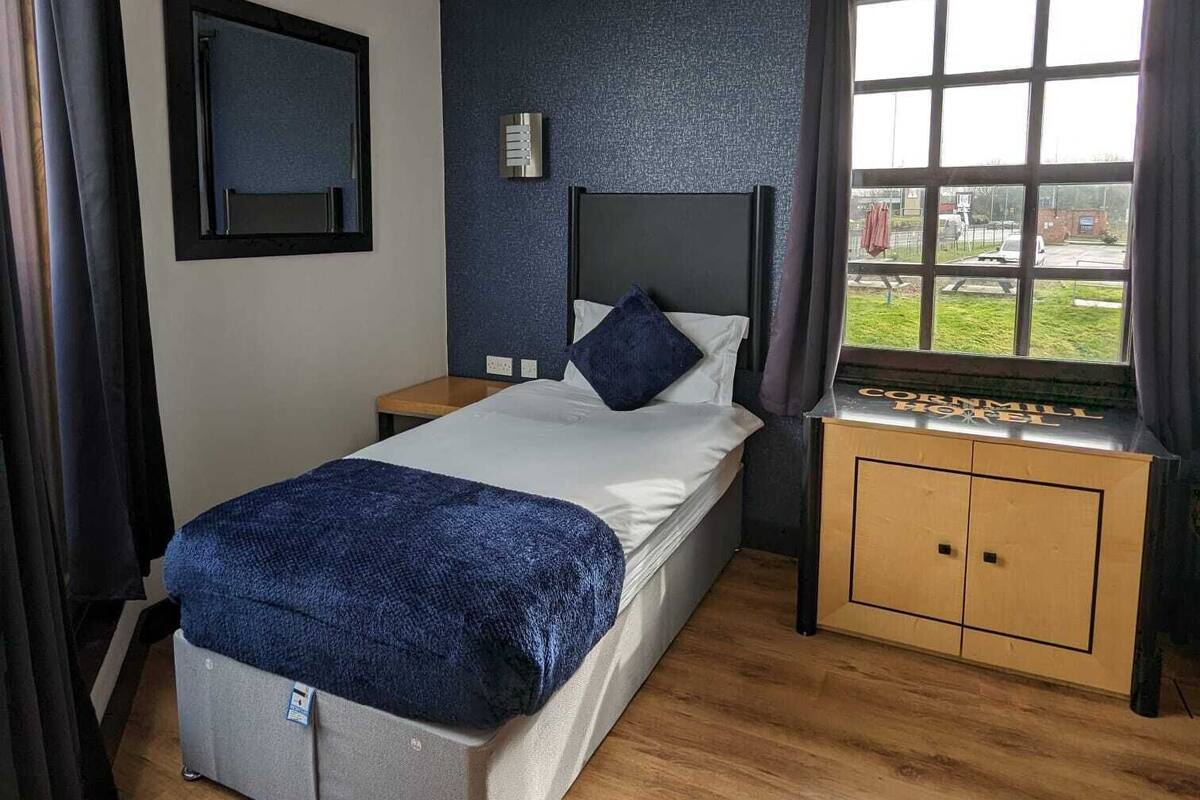 Hotelkamer met een bed, nachtkastje, raam met gordijnen, een tv aan de muur en een plafondlamp.