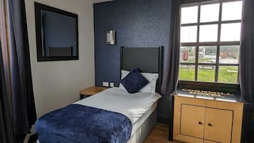 Una habitación de hotel con cama, mesita de noche, ventana con cortinas, televisor montado en la pared y lámpara en el techo.