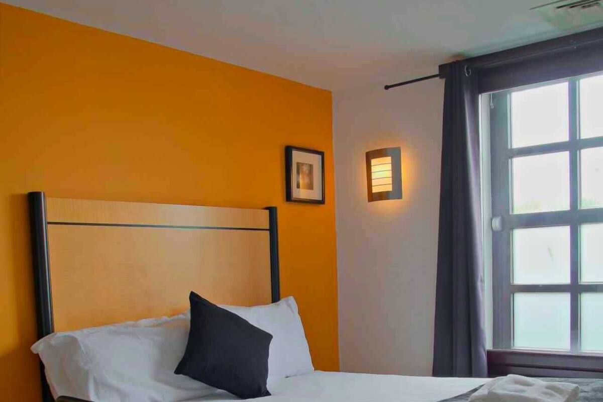 Hotelkamer met een bed, bureau, stoel, raam met gordijnen en een wandlamp.