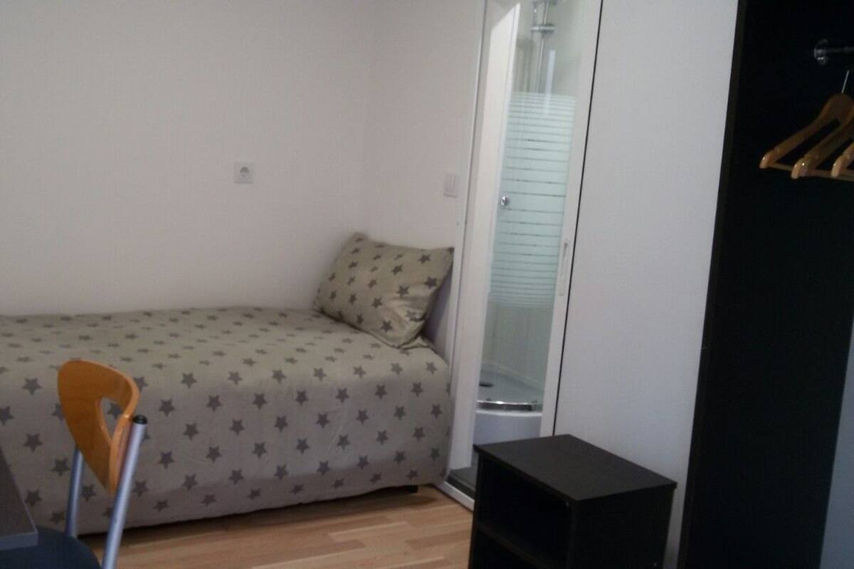 Quarto pequeno com uma cama de solteiro e um edredom estampado com estrelas, uma cadeira de madeira, uma escrivaninha e um armário preto.