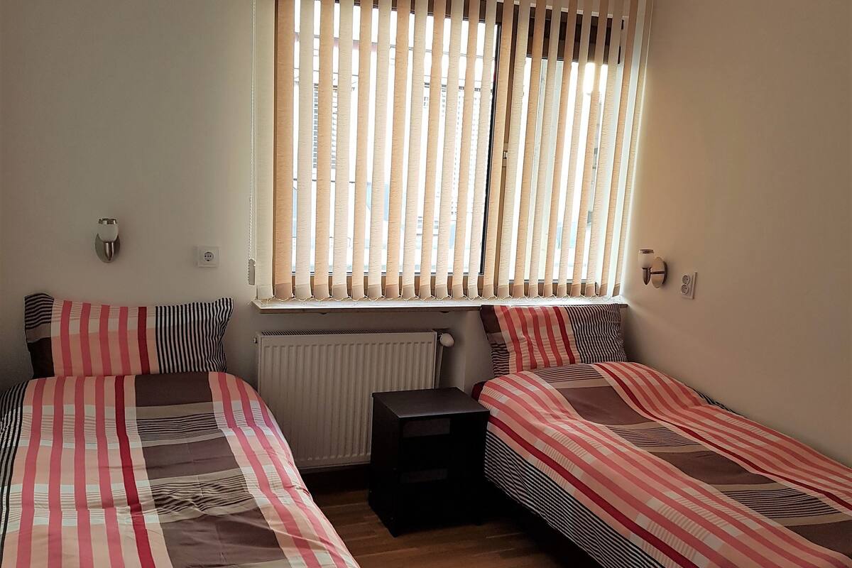 Quarto com duas camas, um radiador e uma janela com persianas.