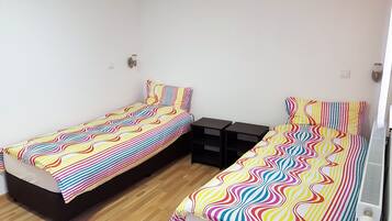 Una habitación con dos camas individuales, cada una con un edredón colorido a rayas. Hay dos mesitas de noche negras con cajones, y un radiador blanco en la pared derecha.