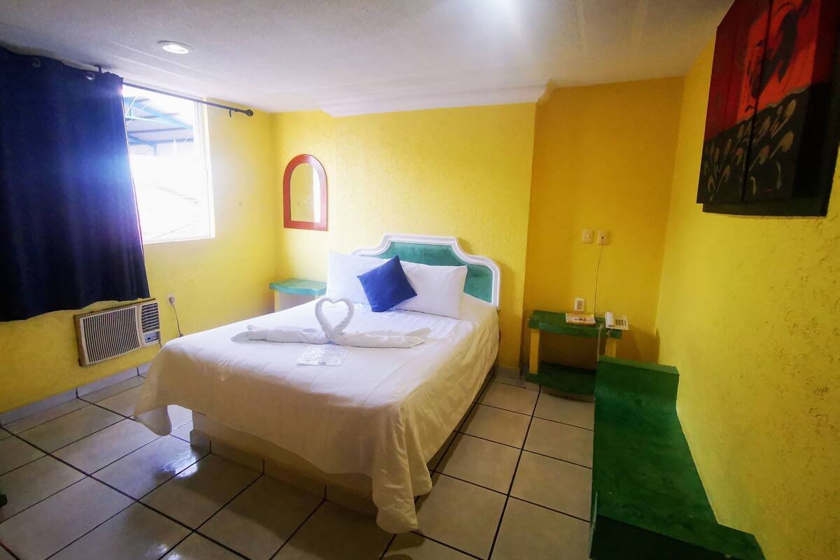 A hotel room with a bed, a nightstand, a mirror, and a wall with a painting.