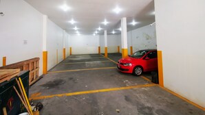 A parking garage with concrete floors, white walls, and orange and white pillars. A red car is parked in one of the spaces.